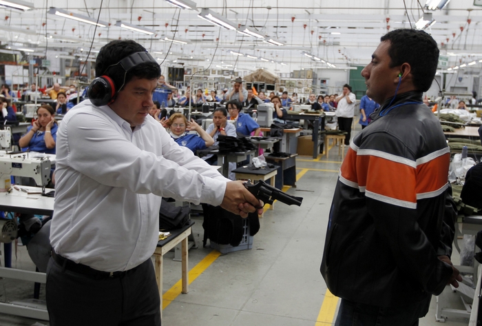 Мигель Кабальеро, президент компании Miguel Caballero Company, стреляет из револьвера 38 калибра для демонстрации прочности бронированной одежды, которую производит его фабрика