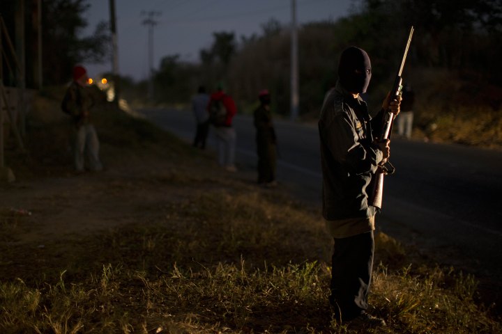 Вооружённый человек в маске охраняет блокпост на въезде в Круз Кемада