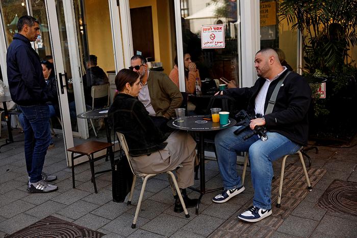 Чоловік із гвинтівкою на колінах сидить на терасі кафе в Тель-Авіві, Ізраїль, 8 лютого 2024 року. Фото: Reuters