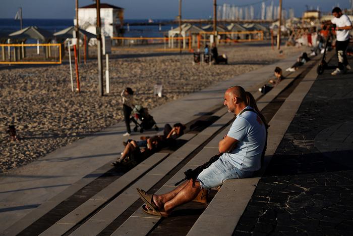Чоловік тримає гвинтівку на колінах, насолоджуючись сонячним днем на пляжній набережній у Тель-Авіві, Ізраїль, 8 лютого 2024 року. Фото: Reuters