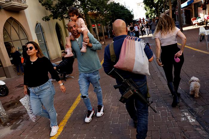 Люди проходять повз чоловіка з гвинтівкою в Тель-Авіві, Ізраїль, 9 лютого 2024 року. Фото: Reuters