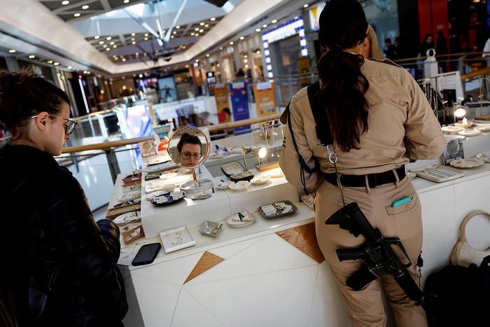 Військова із гвинтівкою робить покупки в ювелірному кіоску торгового центру в Тель-Авіві, Ізраїль, 11 лютого 2024 року. Фото: Reuters 